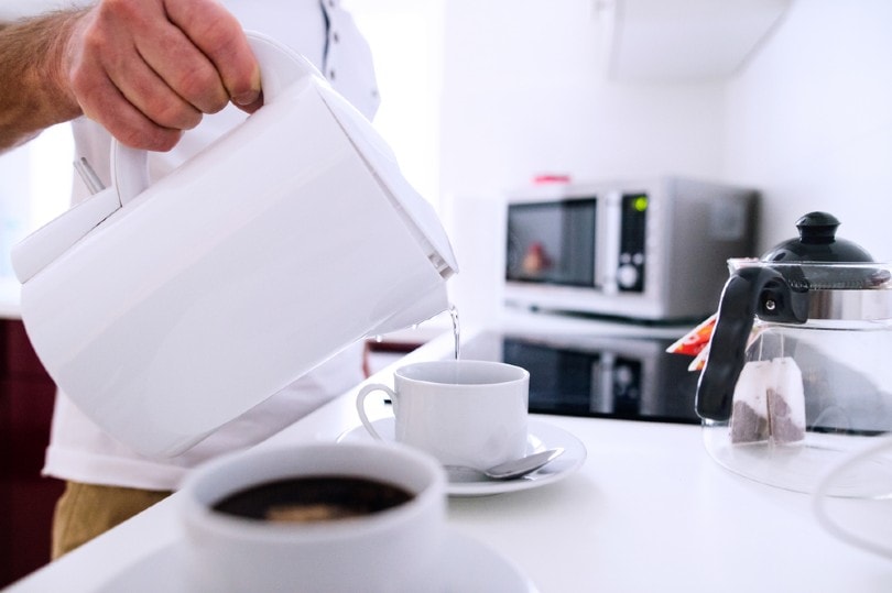 man pouring hot water from electric kettle to the cup