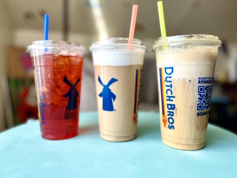 three Dutch Bros drinks with different colored straws on table