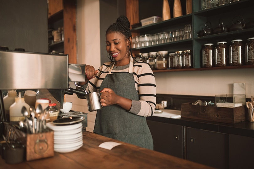 smiling young barista frothing milk for a cappuccino behind the counter