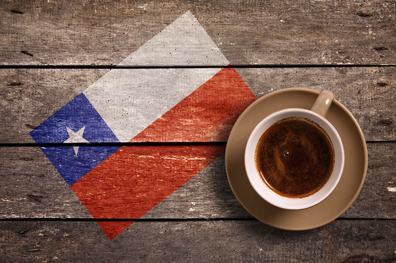 a cup of coffee on a saucer on a wooden table with the flag of chile