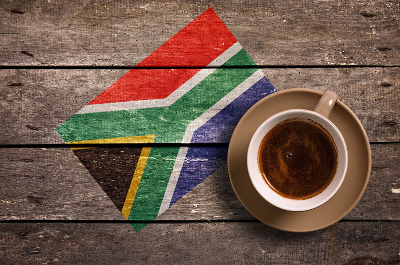 a cup of coffee on wooden surface with the flag of South Africa