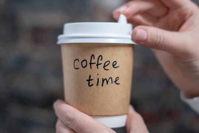 hand holding paper cup of coffee with sleeve