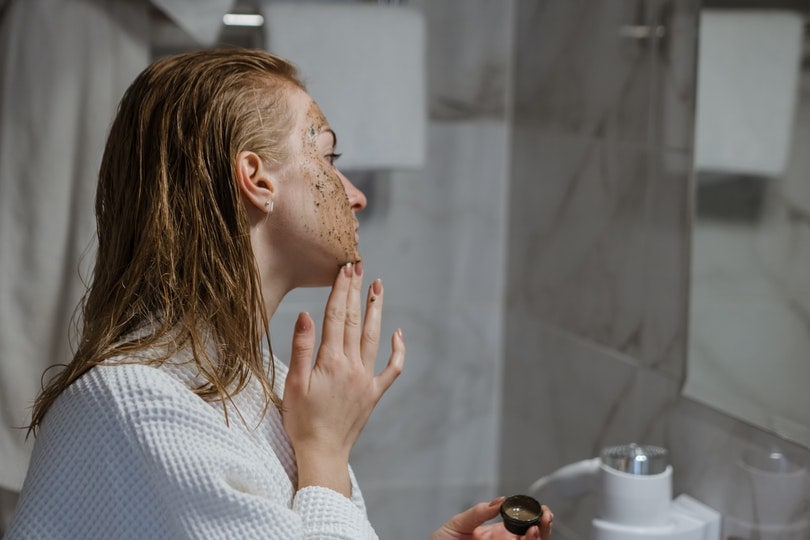 woman applying coffee scrub on face in front of a mirror