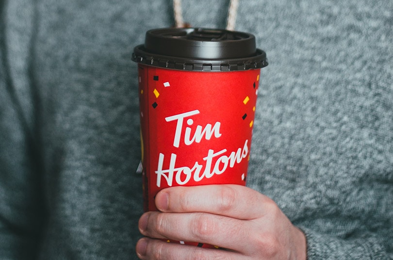 a cropped man holding a cup of tim horton's coffee