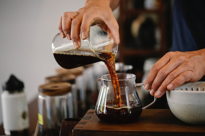 Kurz geschnittener Mann, der Kaffee in einen Glaskrug gießt