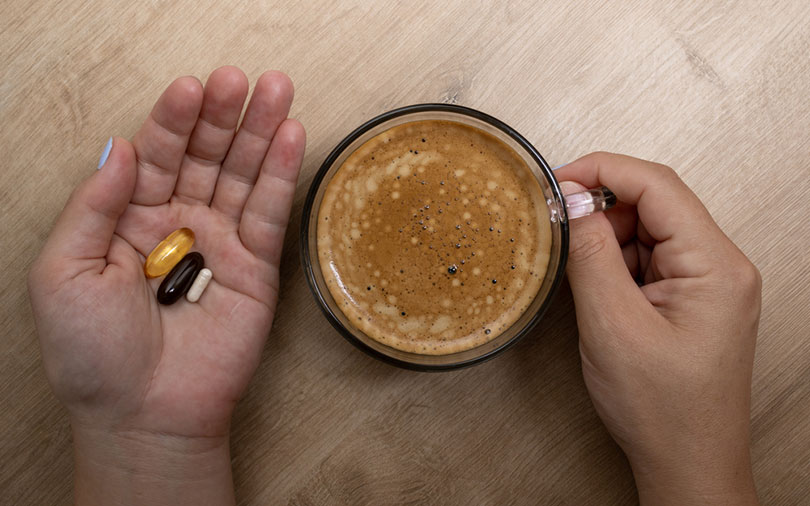 woman holding a combination of medicines and vitamins in her left hand and coffee in a cup in her right hand