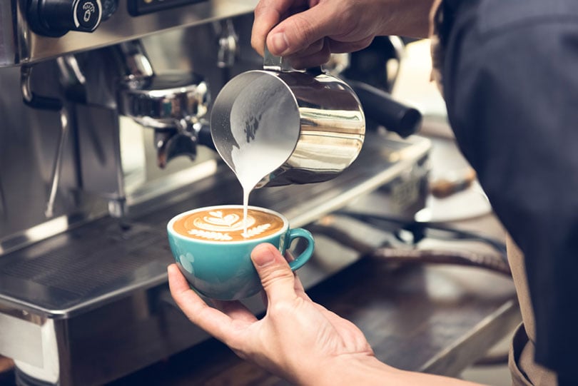 barista nalievajúci dusené mlieko do šálky kávy a robí krásne latte art
