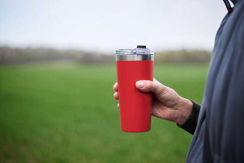 male hand holding red travel mug