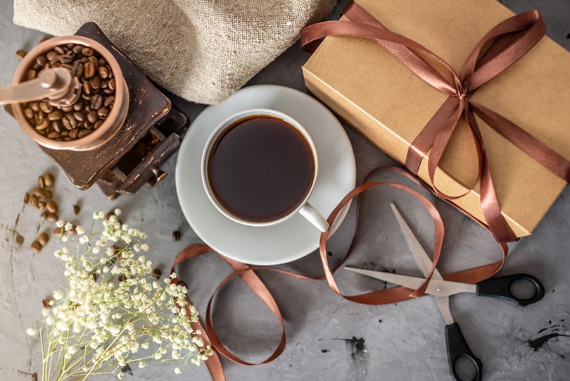 a cup of freshly brewed black coffee, coffee beans in grinder and gift box