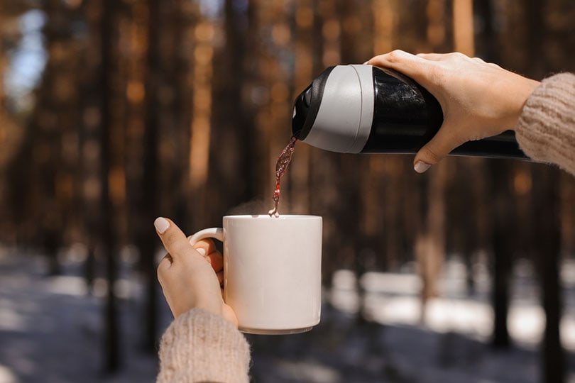 a woman's hands pouring tea from a travel mug