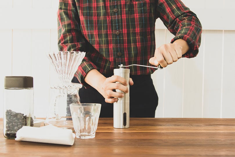 barista is grinding coffee beans with manual stainless steel grinder