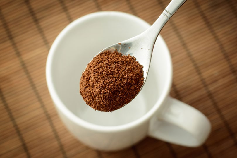 spoon with ground coffee over the white empty cup