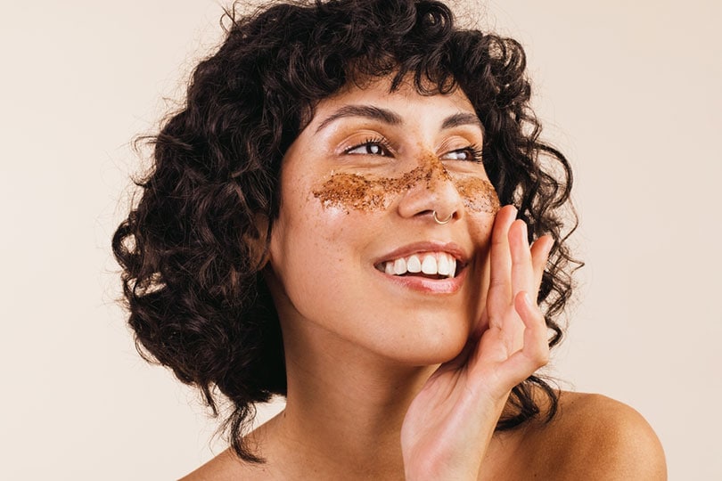 young woman applying coffee scrub on her face