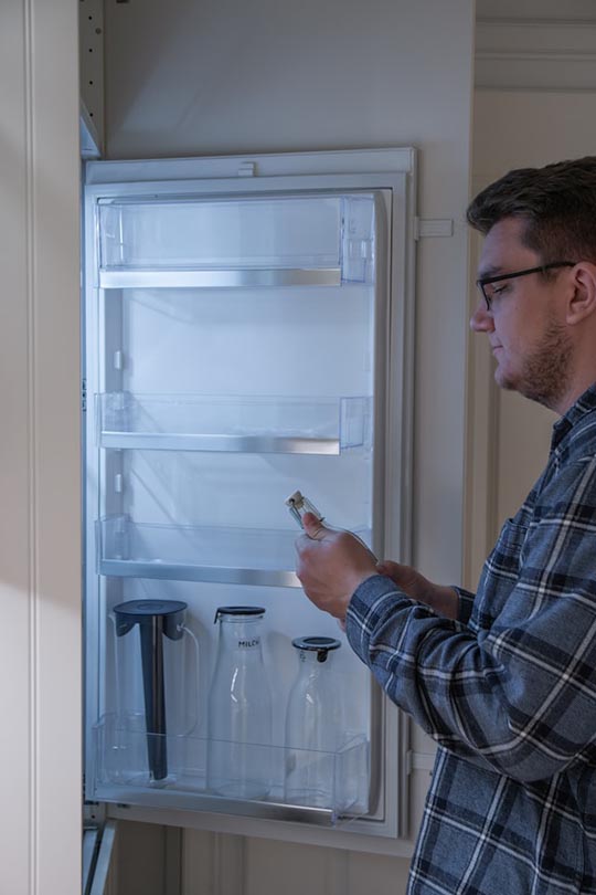 mann setter en flaske til kjøleskapet