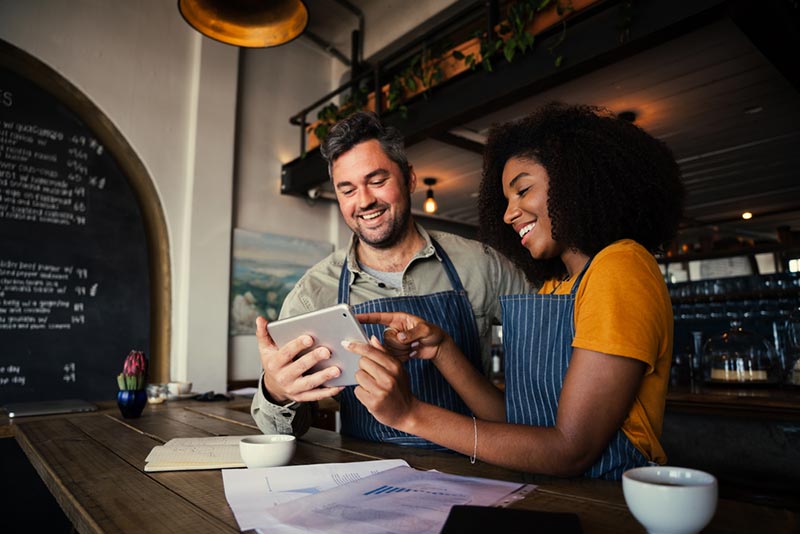 manager and waitress laughing at tablet in cafe