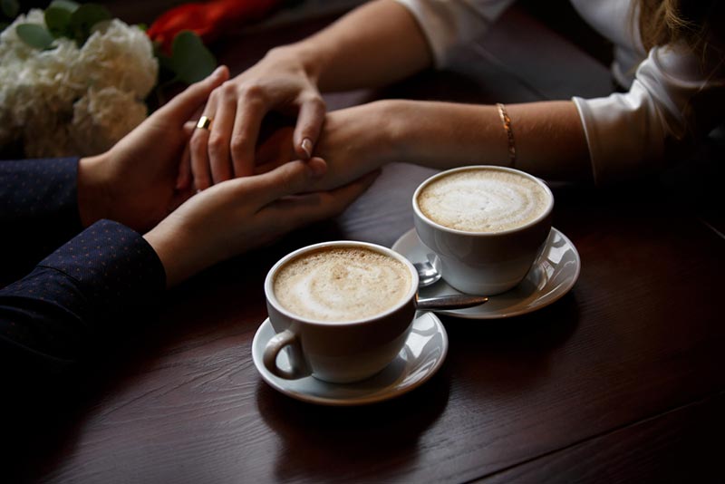 two cups of coffee and hands of couple on date