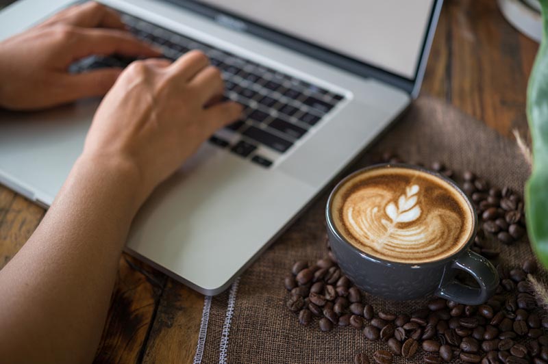 wanita bekerja pada komputer riba dengan secawan kopi latte