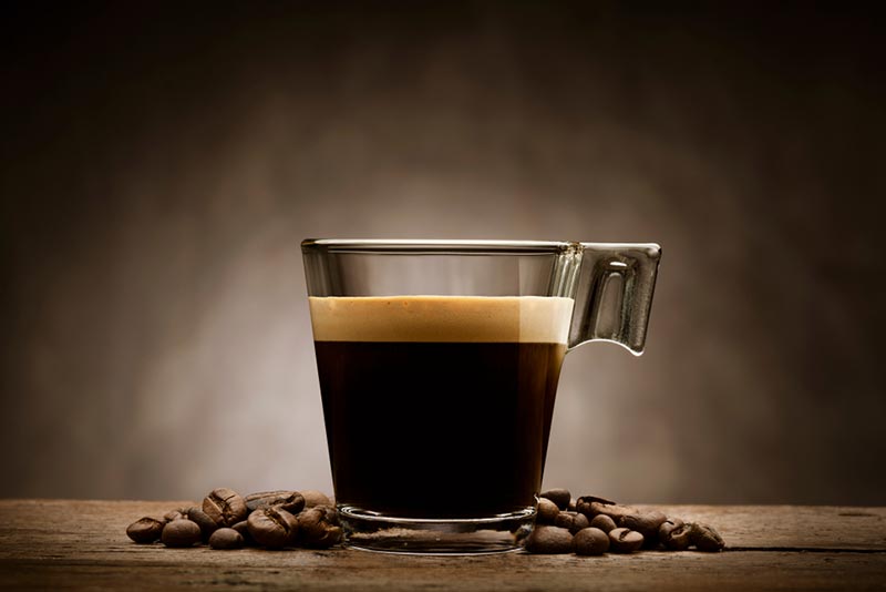 caffè nero in tazza di vetro con chicchi di caffè sulla tavola di legno