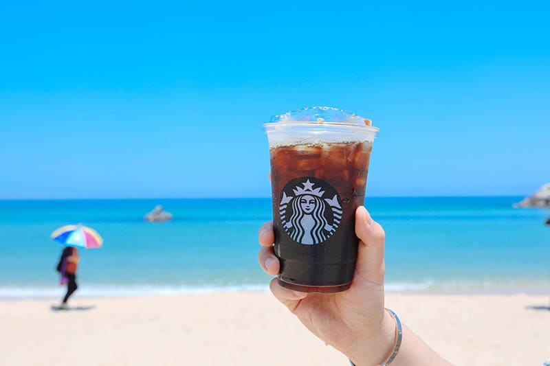 hand holding an iced coffee at the beach