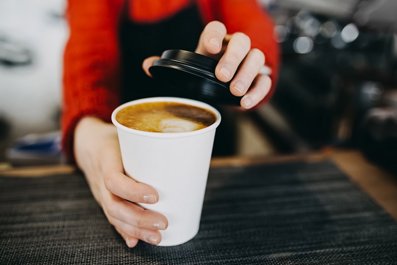 barista holding a hot coffee in paper cup